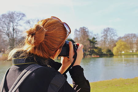 woman in black jacket taking picture of lake