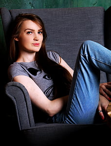 woman wearing gray shirt and blue denim jeans sitting on gray sofa chair