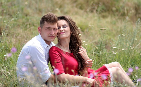 woman and man near each other while sitting on grass field during daytime