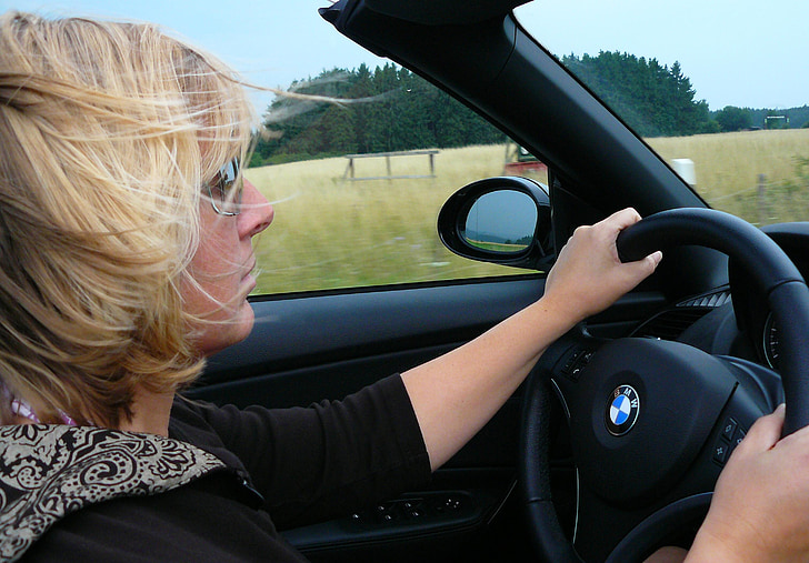 woman in black shirt driving a BMW car near green fields