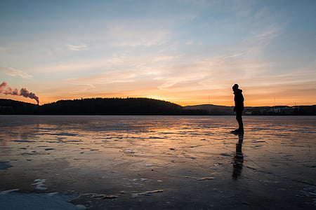 silhouette photo of person standing near body of water during sunset