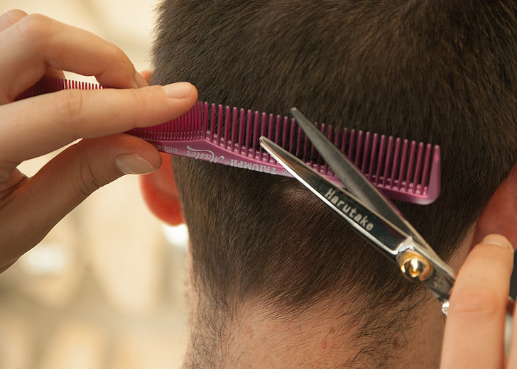 person cutting person's hair using scissors and comb