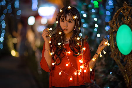 woman wearing red long-sleeved top holding string lights selective focus photography