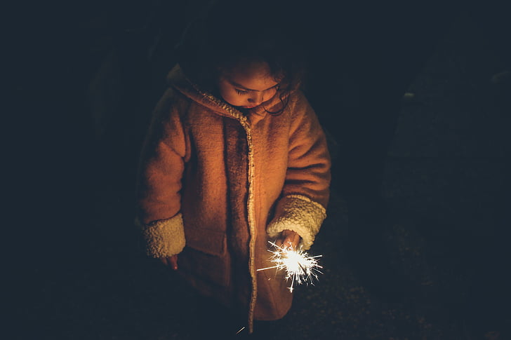 girl in brown coat holding lighted sparkler during nighttime