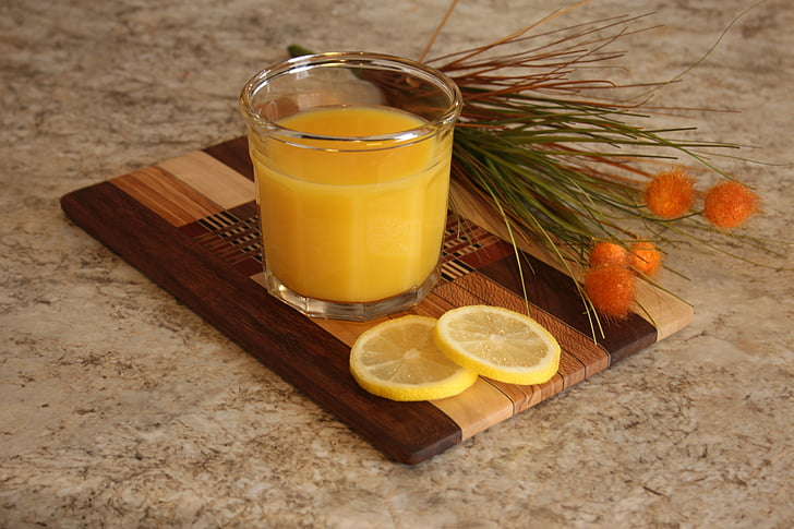 clear drinking glass with fruit juice and sliced lemon on brown wooden board