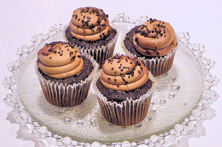 four black-and-brown cupcakes on glass tray