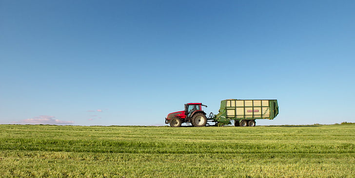 red tractor with green trailer on wide grass field