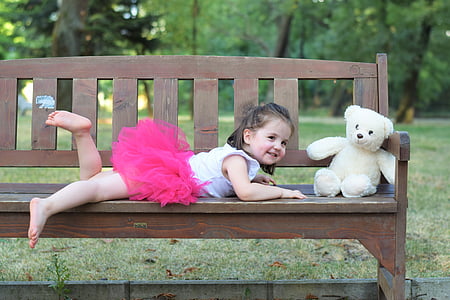 baby wears pink tutu skirt near white bear on brown wooden bench