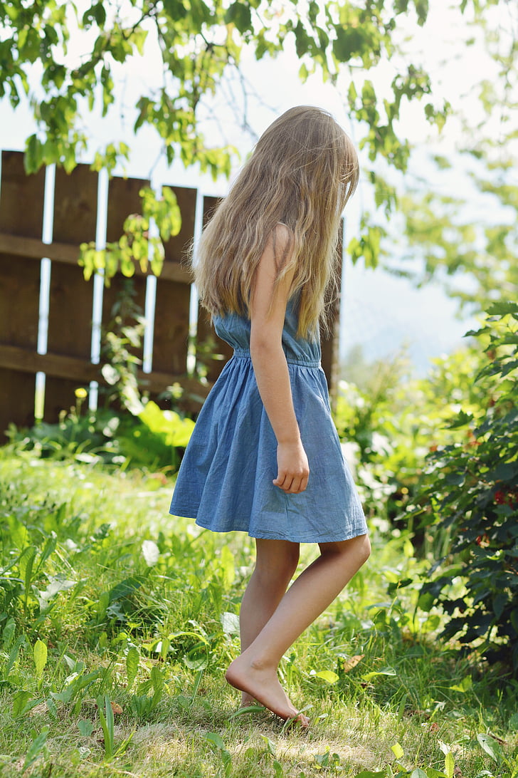 girl in blue chambray dress stands on green grass field at daytime