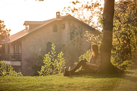 woman sitting under tree far at the house during daytime photography