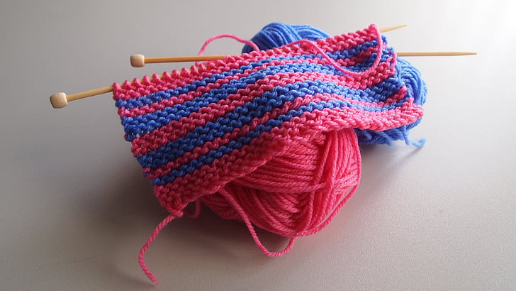 pink and blue knitted yarns with stitching needles on to of white flooring