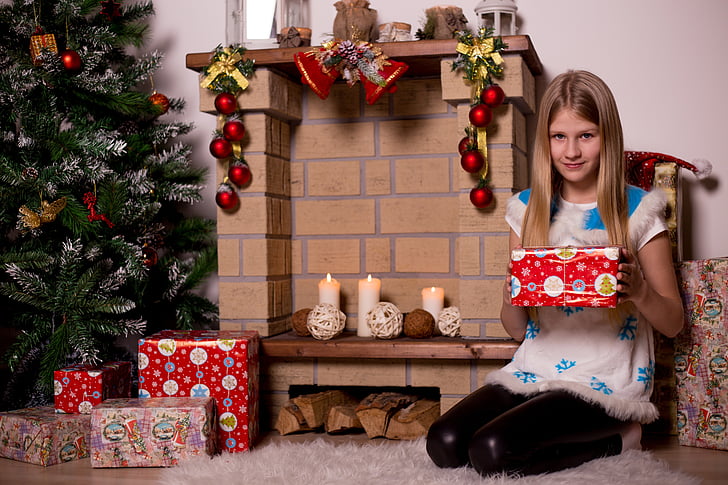 girl holding a Christmas gift near fireplace mantel