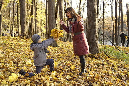 boy holding flowers kneel in front of woman in middle of trees