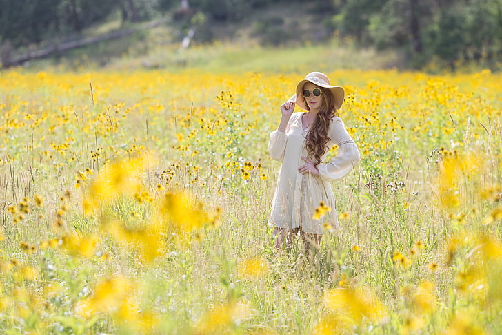 woman in white long-sleeved dress and hat standing in field of yellow flowers