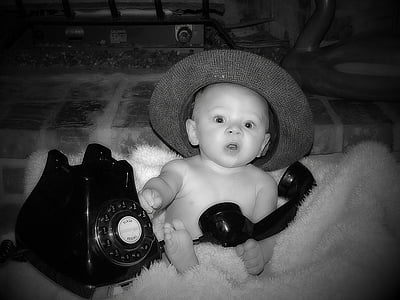 baby sitting on fur rug beside rotary telephone on grayscale photography
