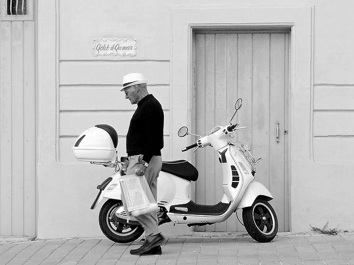 grayscale photography of man standing near motor scooter