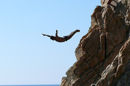 man jumps from rock towards the ocean