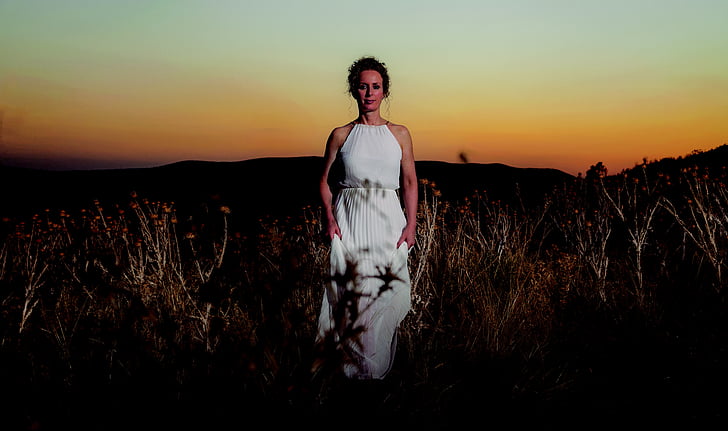 woman standing on grass wearing white dress during dawn