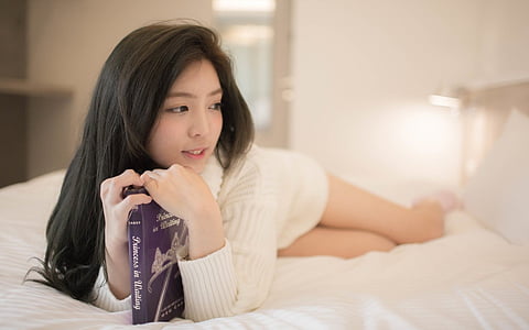woman wearing white sweater lying on bed