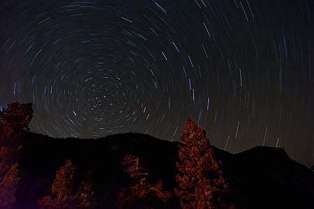 time-laps photography of star filled sky over trees and mountains at the distance