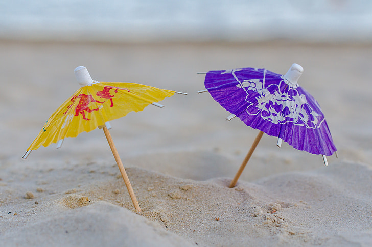 micro photography of two assorted-color mini umbrellas on sand