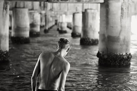 grayscale photography of man walking on water under bridge