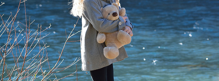 woman holding brown teddy bear near river