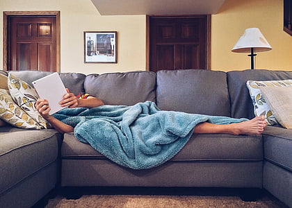 person covered with blue blanket lying on gray sofa