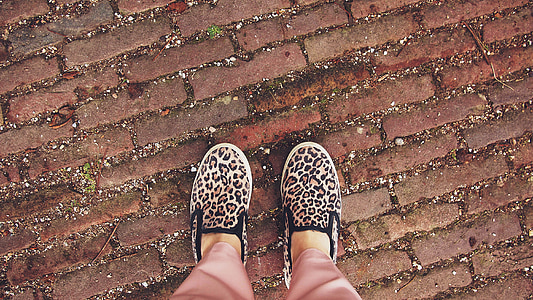 person wearing beige-black-and-pink leopard print slip-on shoes over red brick ground