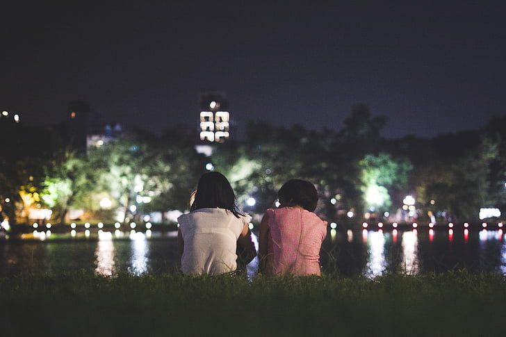 two woman seats on green grass at nighttime