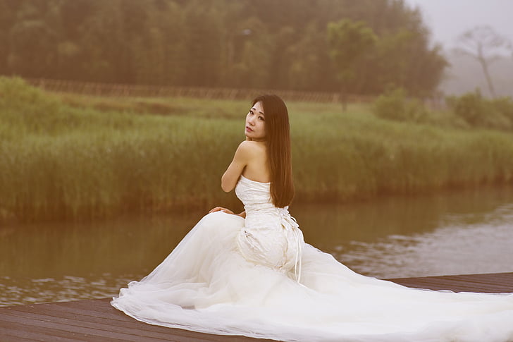 woman wearing white dress kneeling beside lake