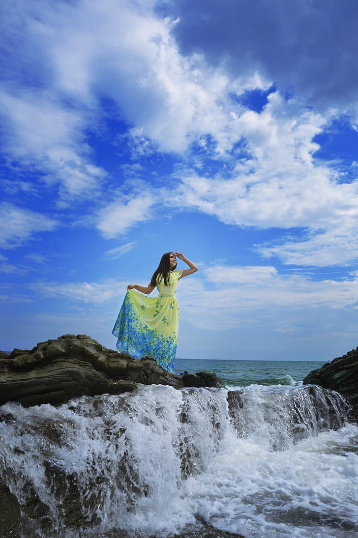 woman standing on rock formation surrounded with water under cumulus cloud