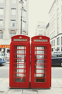 two vintage red telephone booths beside sidewalk