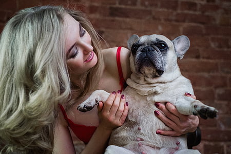 woman wearing red spaghetti strap top carrying French bulldog