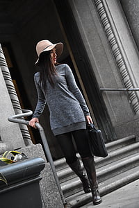 woman in gray sweater and black leggings holding handbag walking downstairs