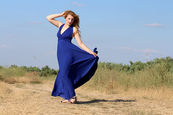 woman wears blue halter dress dancing outdoor during daytime