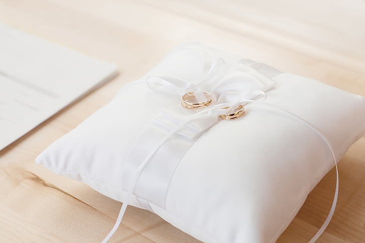 two gold-colored wedding rings on white pillow