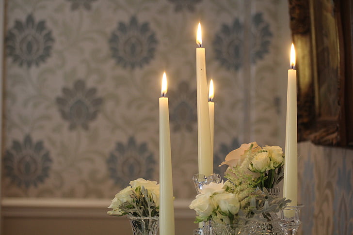 lighted white taper candles beside white rose flowers bouquets