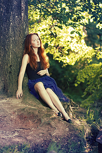 woman in black sleeveless top and blue skirt sitting under the tree