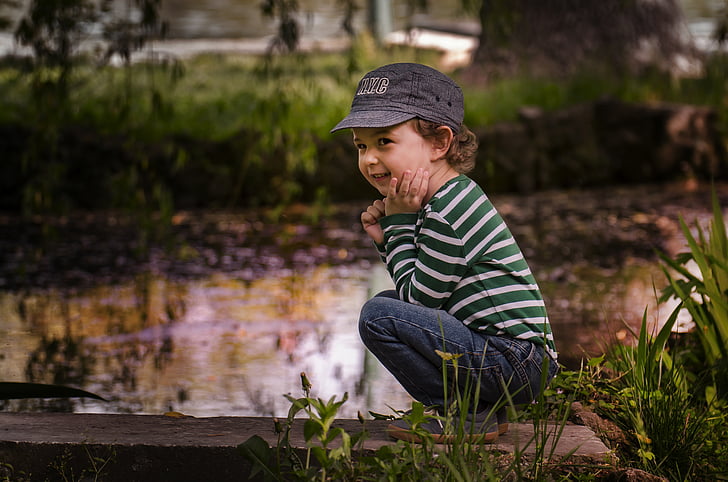 selective focus photo of a boy squatting near body of water