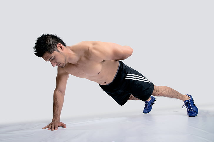 man wearing black Adidas shorts and blue shoes executing push-up with one hand