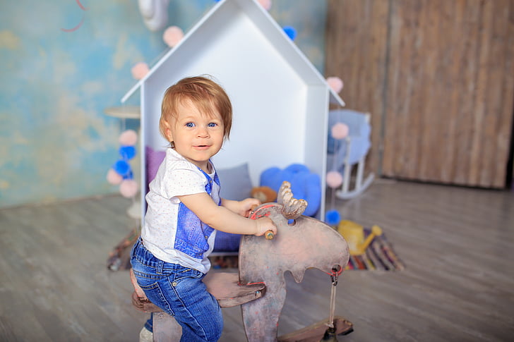 toddler wearing white and blue riding brown animal toy