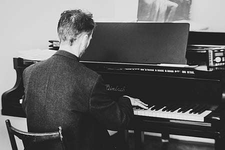 grayscale photo of man playing grand piano