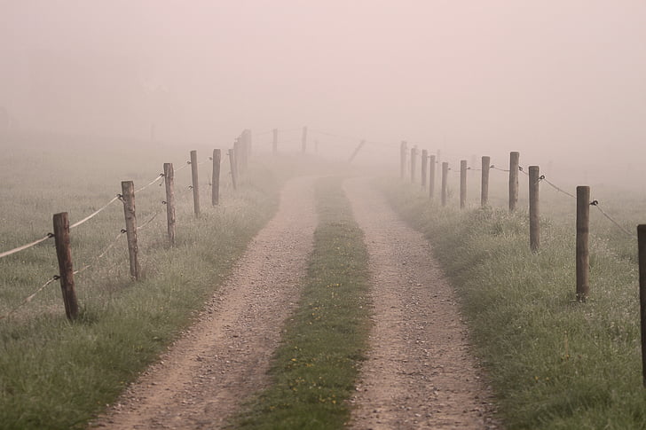 landscape photo of dirt road with brown wood posts by the road under foggy sky