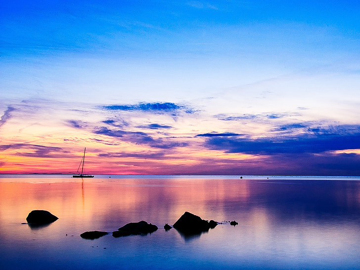 silhouette photo of boat and rock in calm body of water at sunset