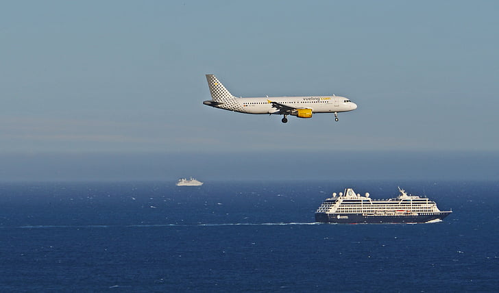white airliner above ocean near cruise ship