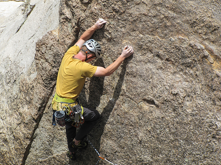 man wearing yellow shirt climbing on rock