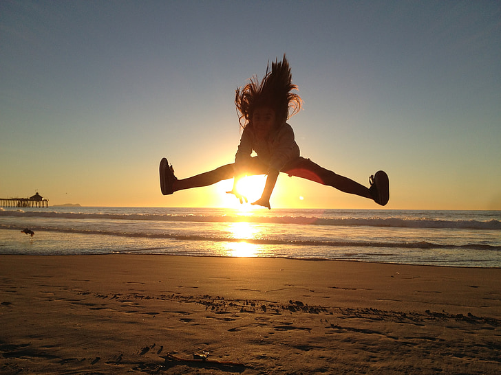 girl jumps on seashore during sunset