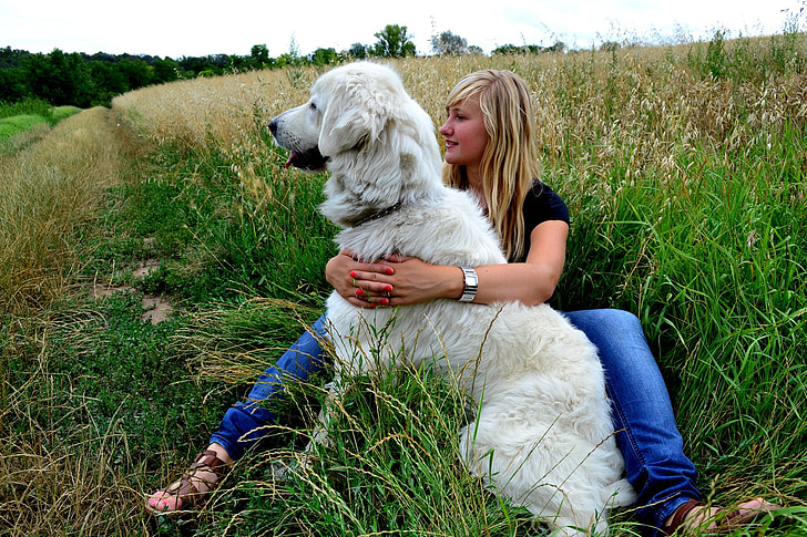 woman wearing black shirt hugging dog while sitting on grasses