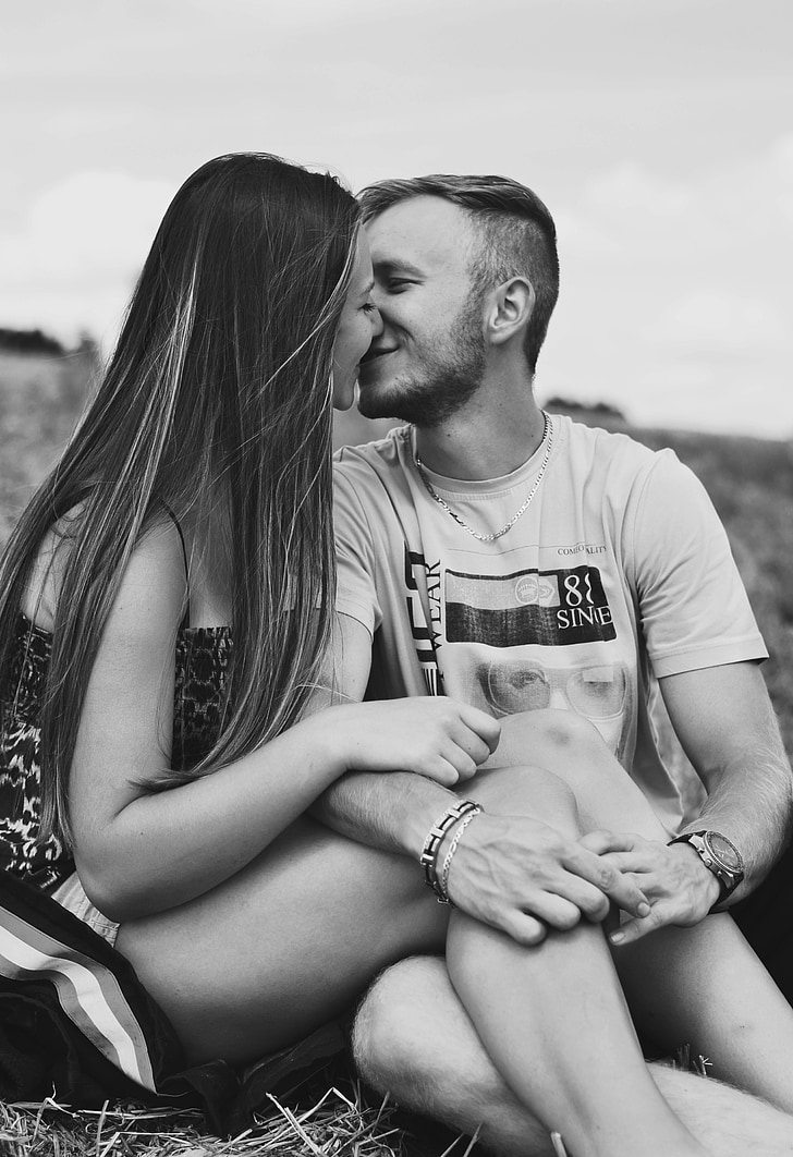 grayscale photo of couple kissing while sitting on grasses